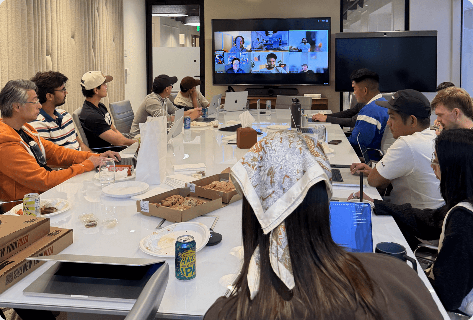 The Collective team meeting around a table, with remote teammates on screen
