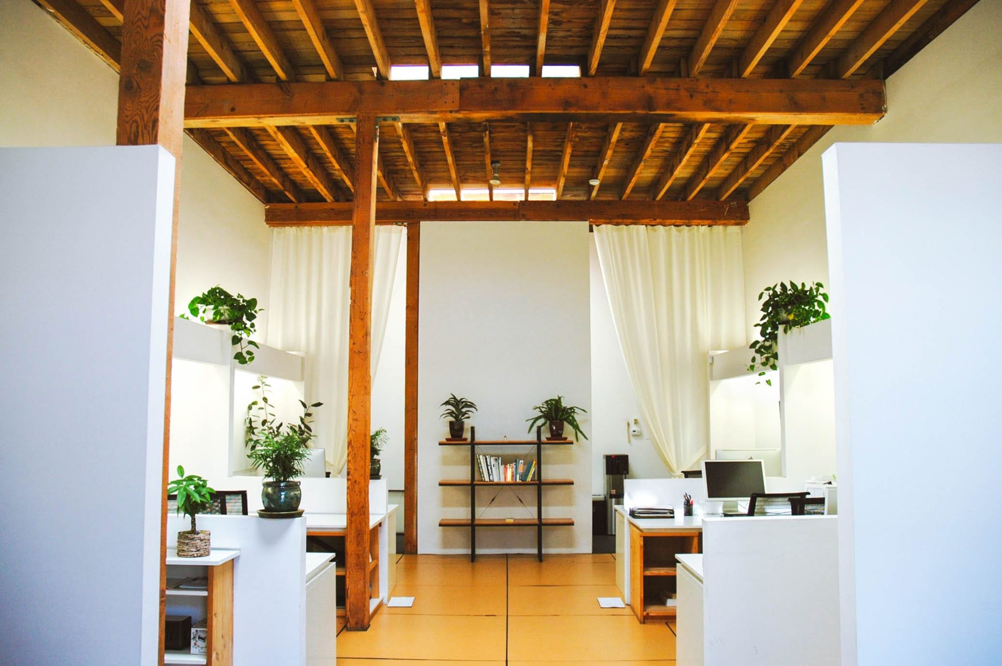 Image of inside a studio space. There are wooden beams on the veiling, and white desks lining the walls.