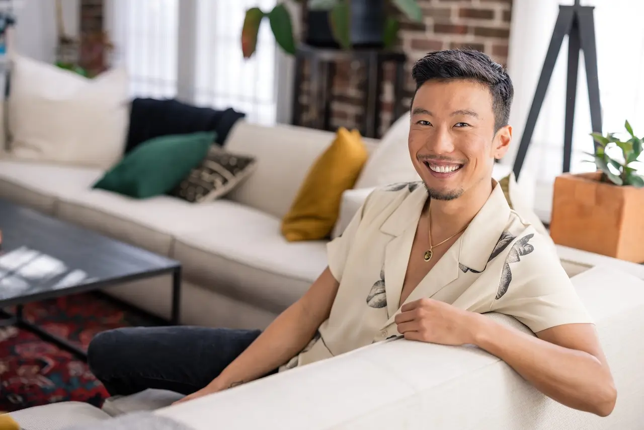 Portrait of Collective member Scott Shigeoka, Author & Public Speaker, sitting on a couch and smiling at the camera