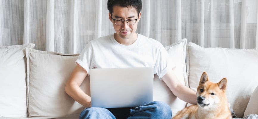 Asian man working on laptop at home with dog