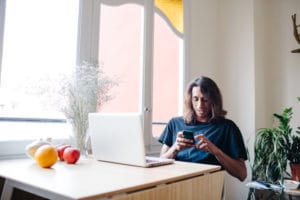 Long haired brunet man using smatphone while sitting at the table near window
