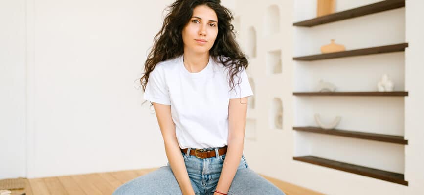 Stylish woman with curly hair in jeans sitting on a chair in studio.