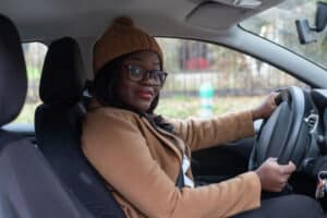 portrait of smiling black woman looking at camera in the car, wearing winter clothes, driving on the road