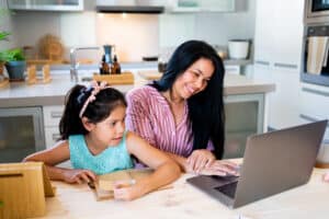 Portrait of latin american mother with her daughter doing homwork and working with the laptop at modern kitchen
