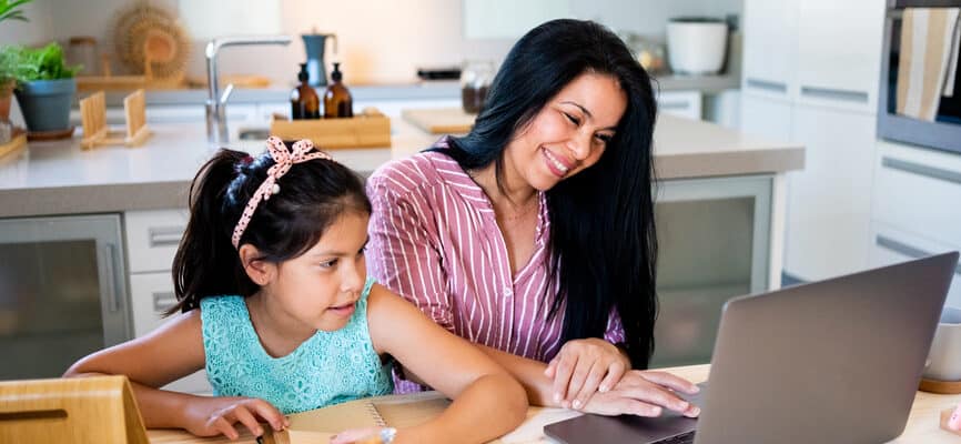 Portrait of latin american mother with her daughter doing homwork and working with the laptop at modern kitchen
