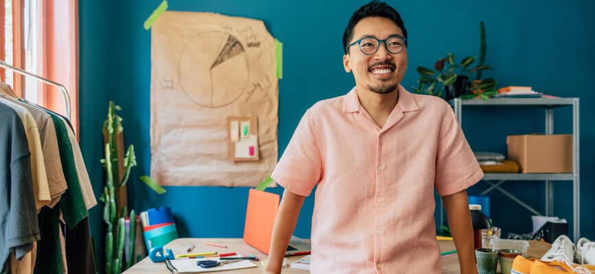 Portrait of handsome asian man standing in front of his work desk in his workshop and smiling